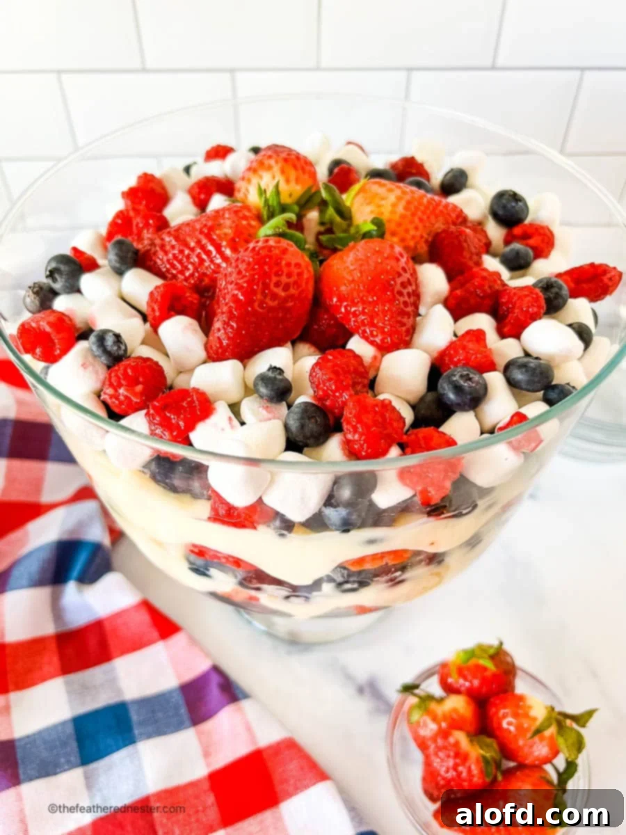 A large, clear serving bowl filled with a beautifully layered Red, White, and Blue Cheesecake Salad, featuring red strawberries, white cheesecake filling, and blue blueberries, set against a festive patriotic tablecloth.