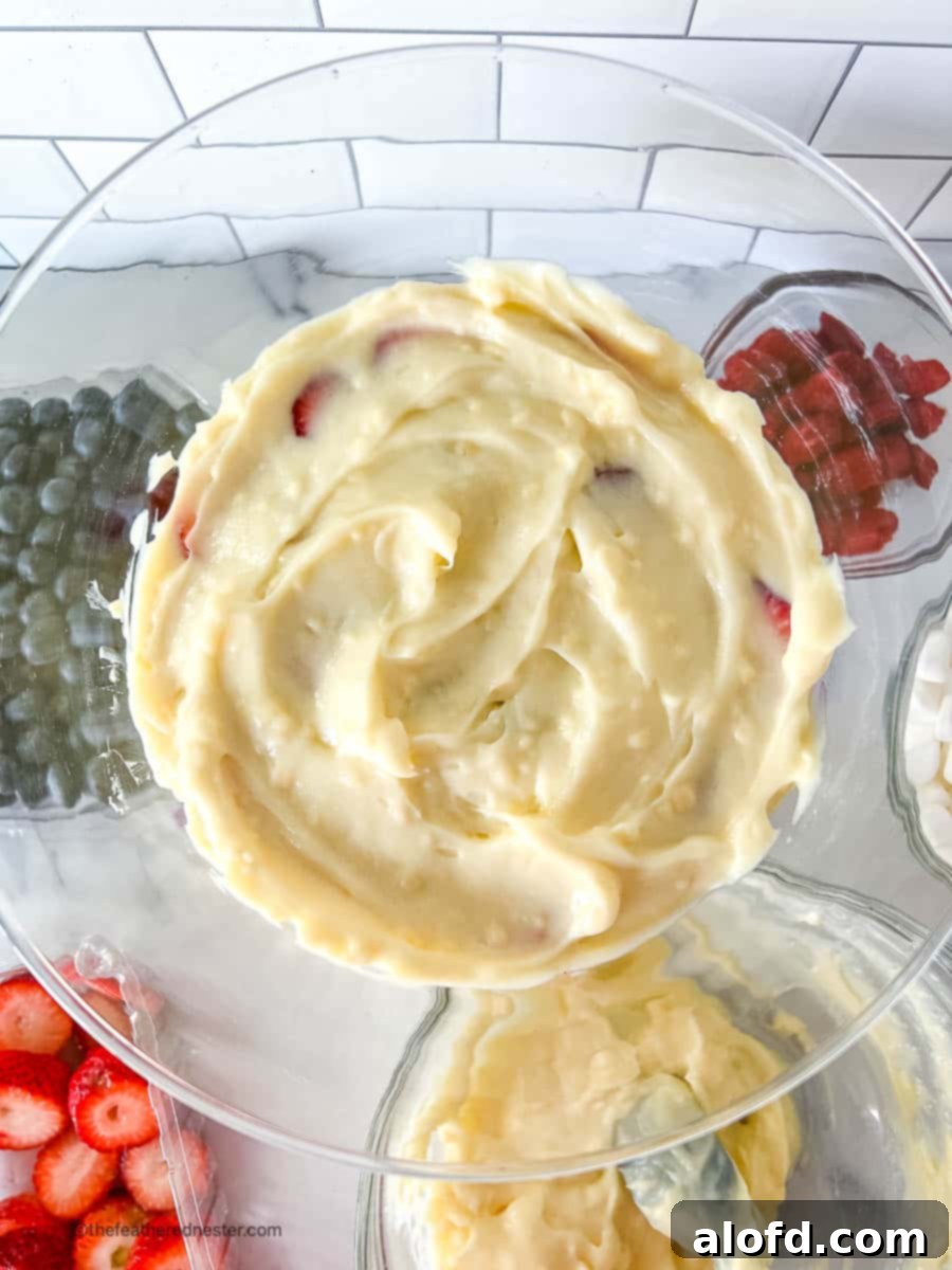 An overhead view of a dessert bowl, showing a smooth white layer of pudding covering vibrant red and blue berries, illustrating a stage in the layering process.