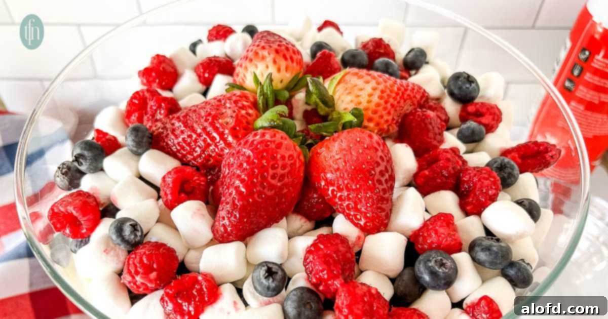 A close-up of mini marshmallows, fresh raspberries, strawberries, and blueberries combined in a clear glass serving bowl, highlighting the colorful ingredients.