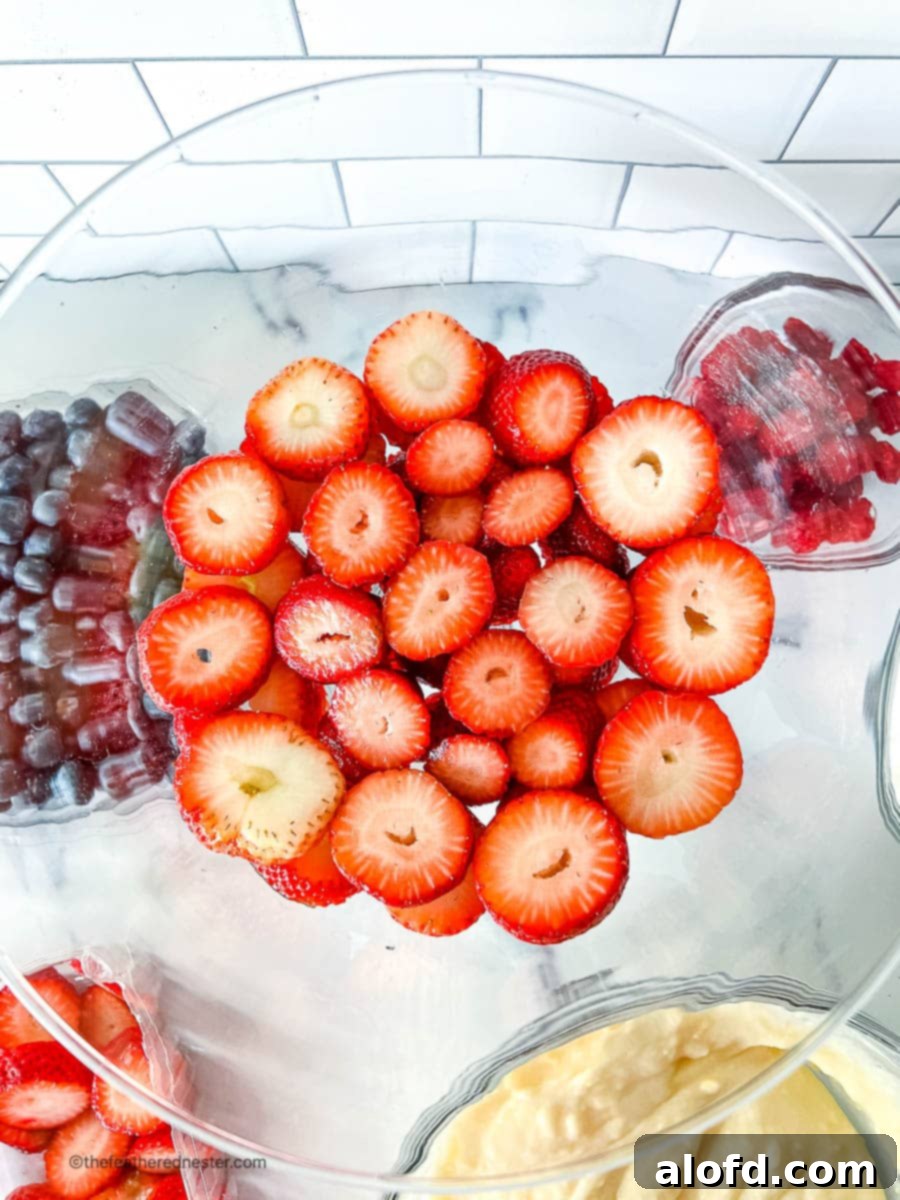 An overhead shot of freshly sliced strawberries meticulously arranged in a clear glass bowl, ready for layering in the cheesecake salad.