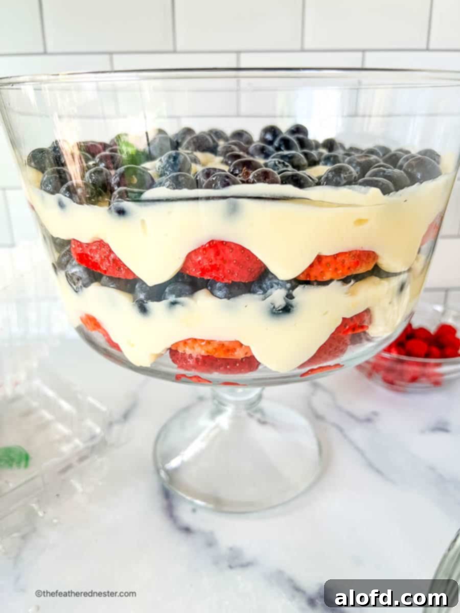 A stunning layered fruit and pudding 4th of July salad beautifully presented in a clear trifle bowl, highlighting the patriotic colors.
