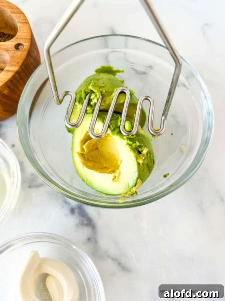 Velvet Avocado Spread 6 Using a potato masher to smash green fruit in a bowl.