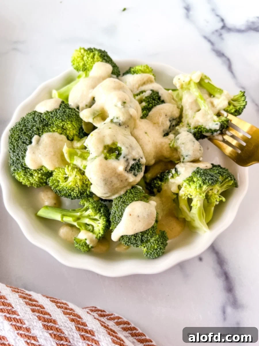 Bowl of Instant Pot steamed broccoli with cheese sauce, and one floret on a fork.
