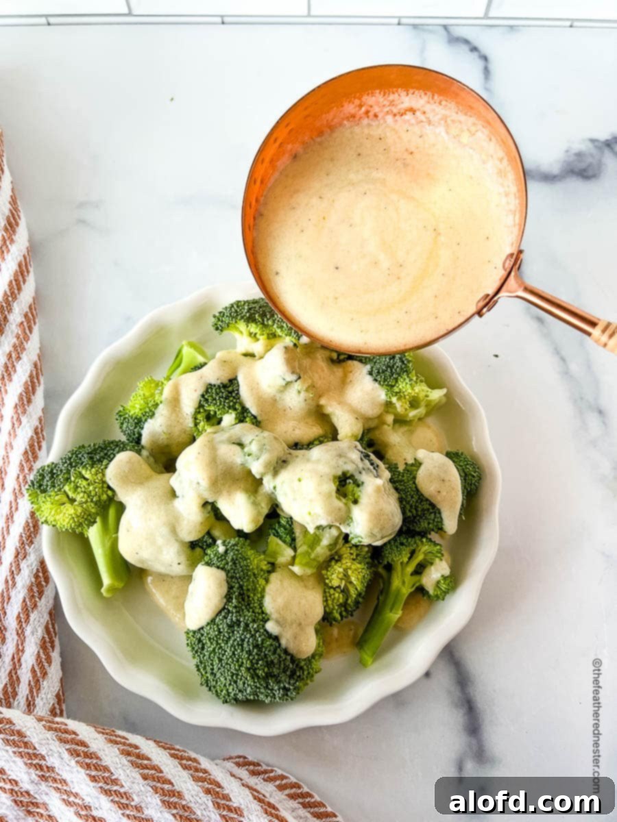 Ladling white cheese sauce over steamed vegetables in a serving bowl.