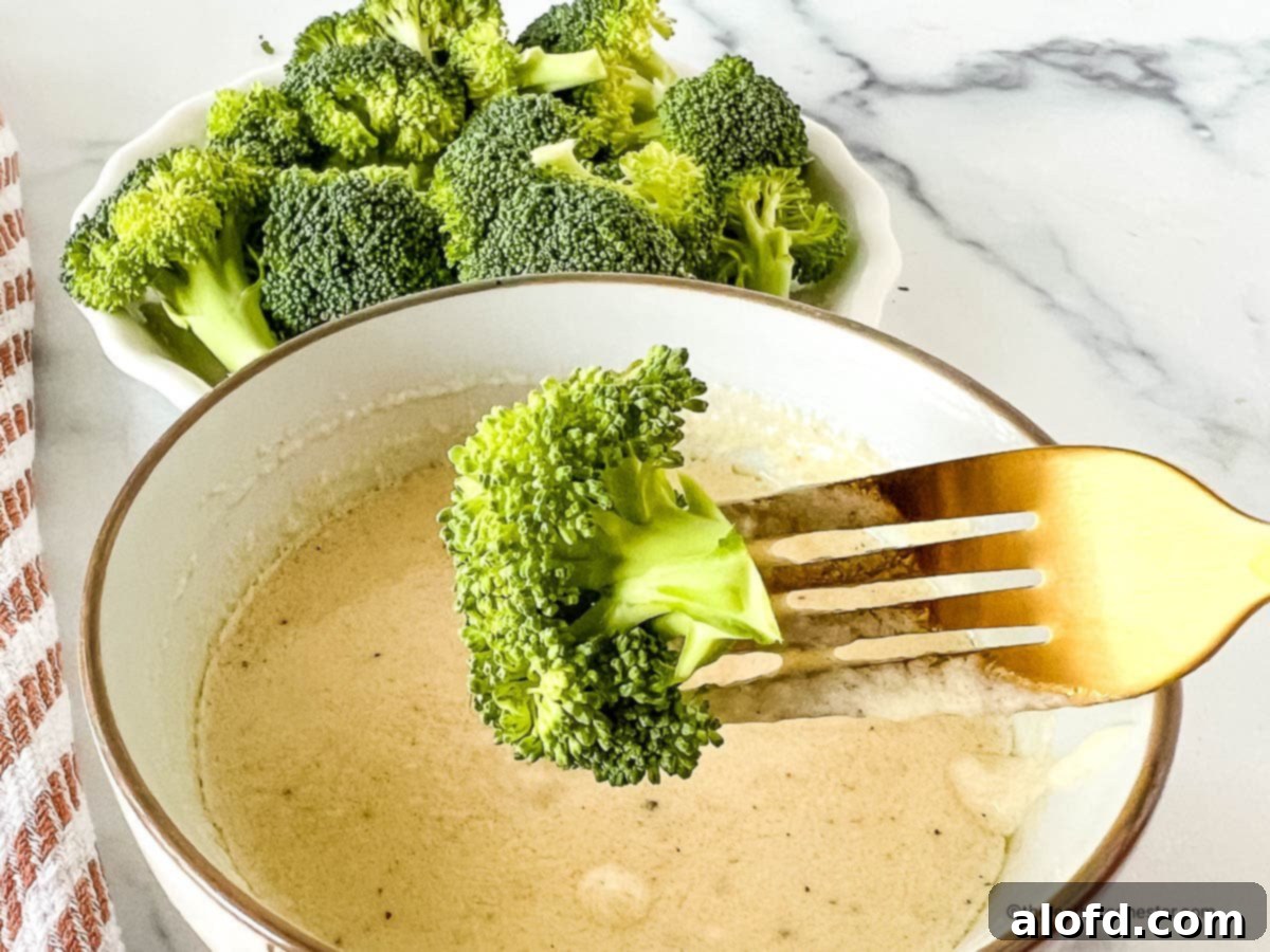 Tender-crisp Instant Pot steamed broccoli florets in a small serving bowl and on a fork above a bowl of cheese sauce.