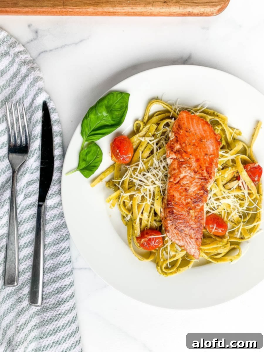 Bright Salmon Pesto Pasta 2 A perfectly plated dish of salmon pesto pasta, showcasing tender salmon fillets, bright green pesto-coated fettuccine, and vibrant blistered cherry tomatoes.