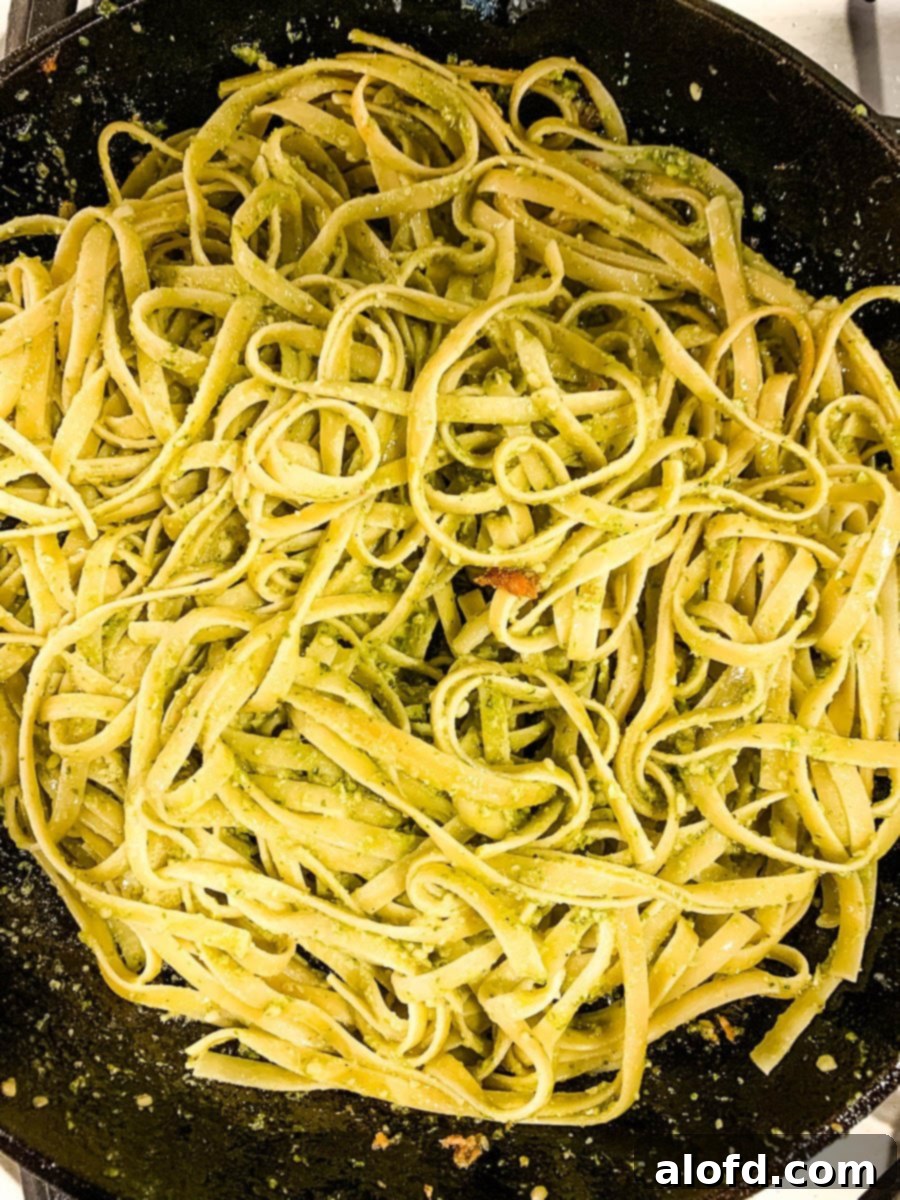 Bright Salmon Pesto Pasta 6 Fettuccine pasta being tossed with vibrant green pesto sauce in a large skillet, ready to be combined with other ingredients.