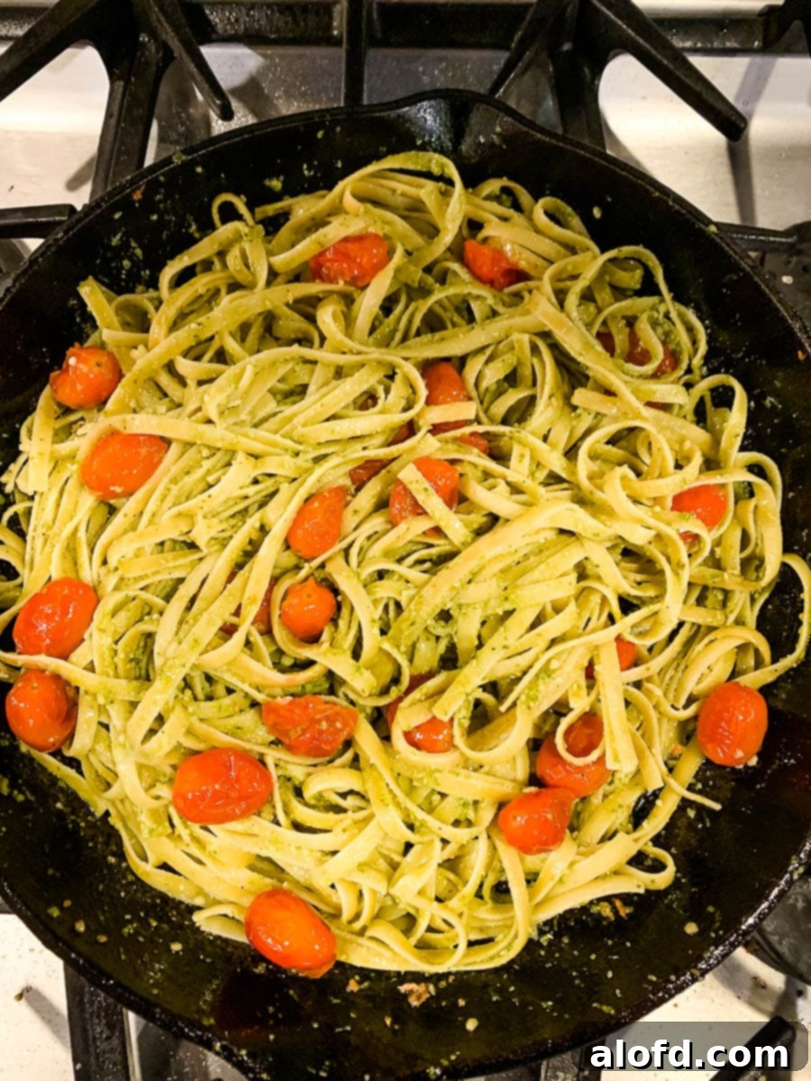 Bright Salmon Pesto Pasta 8 Cooked fettuccine pasta and blistered tomatoes being gently stirred in a skillet, ready for the final sauce combination.