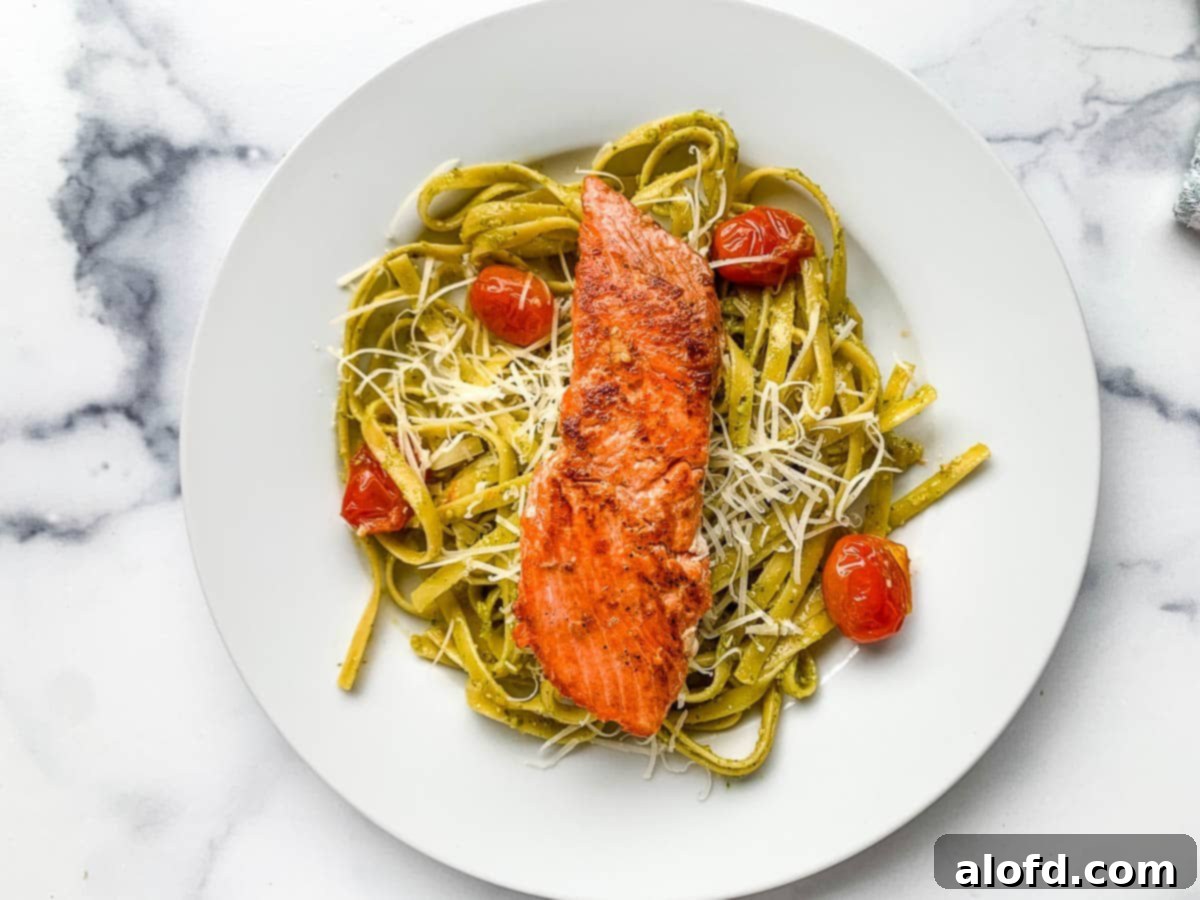 Bright Salmon Pesto Pasta 9 A tantalizing close-up of salmon pesto pasta on a plate, garnished with fresh basil, grated Parmesan, and vibrant blistered tomatoes, ready to be enjoyed.