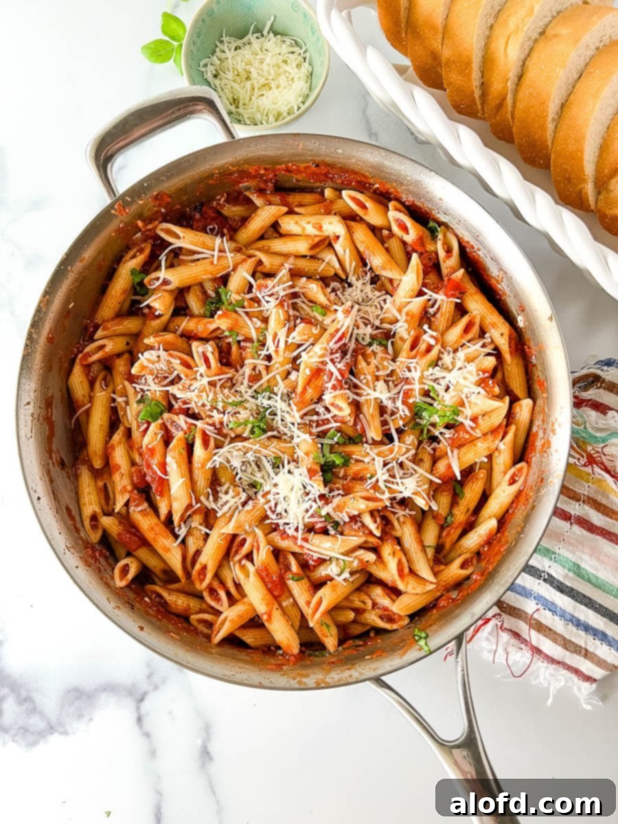 Penne alla Pomodoro in a stainless steel skillet, garnished with fresh basil and Parmesan cheese.