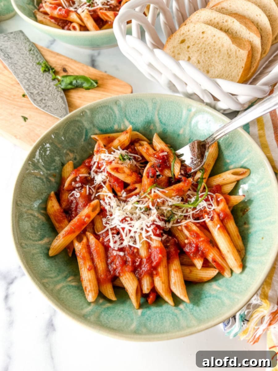 Cooked penne noodles coated with a rich tomato basil pasta sauce and topped with freshly grated Parmesan cheese in a vibrant green bowl.