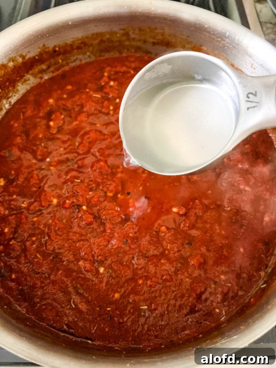 Thinning a red tomato basil pasta sauce with starchy pasta cooking water to achieve the perfect consistency.