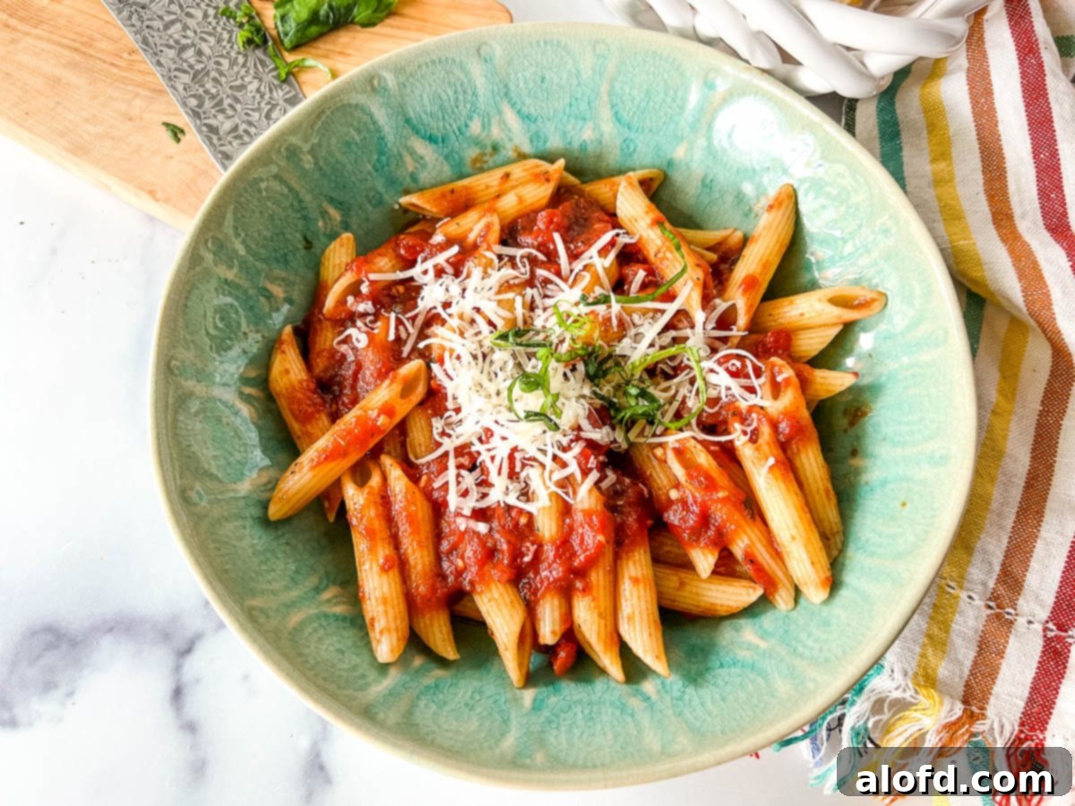 Plated Italian pasta dinner, close up, showing penne al pomodoro garnished with fresh basil and Parmesan cheese.