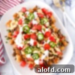 Loaded tater tots on a white platter, generously topped with cheese, beef, and other nacho essentials.