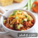 Soup bowl filled with homemade stovetop chili, garnished with shredded cheddar cheese and chopped scallions, ready to be enjoyed.