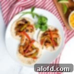 a plate of three Blackstone chicken fajitas on flour tortilla on a white plate with a sprig of cilantro atop a red and white napkin.