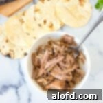 Shredded meat in a small white bowl next to charred tortillas, ready to be assembled into delicious carnitas tacos.