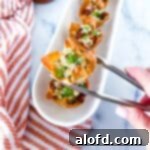 a hand and tong holding a jalapeno popper wonton cup and a serving tray full of jalapeno wonton popper cups and a striped red cloth in the background.