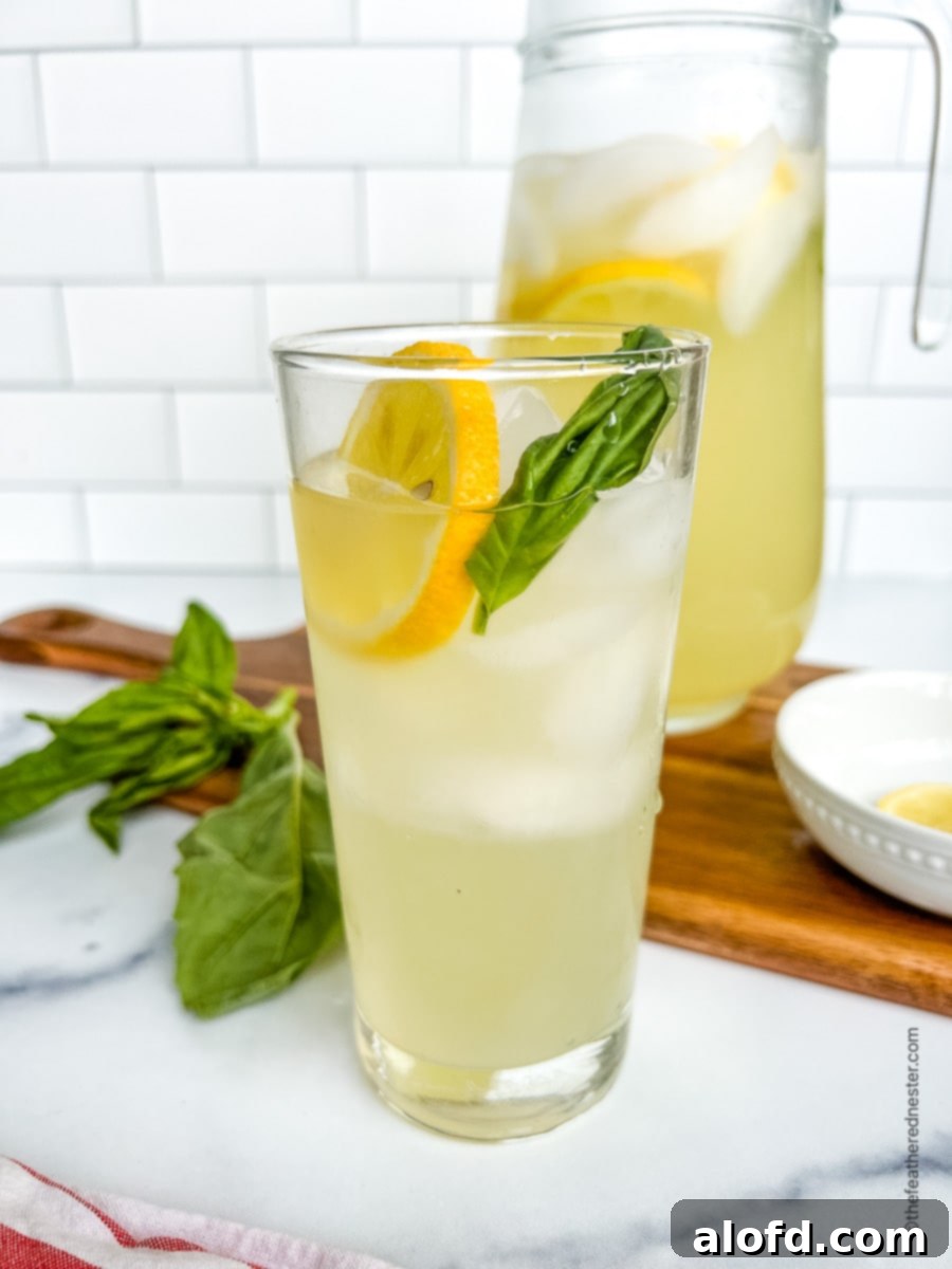 Tall glass of basil lemonade in front of a pitcher full.