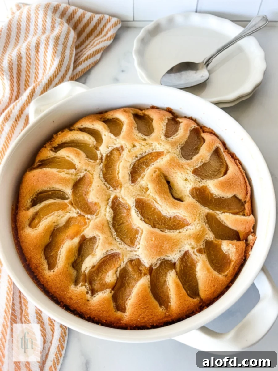 Peach cobbler pound cake baked in a round white baking dish. Stack of dessert plates and spoons sitting behind the pound cake.