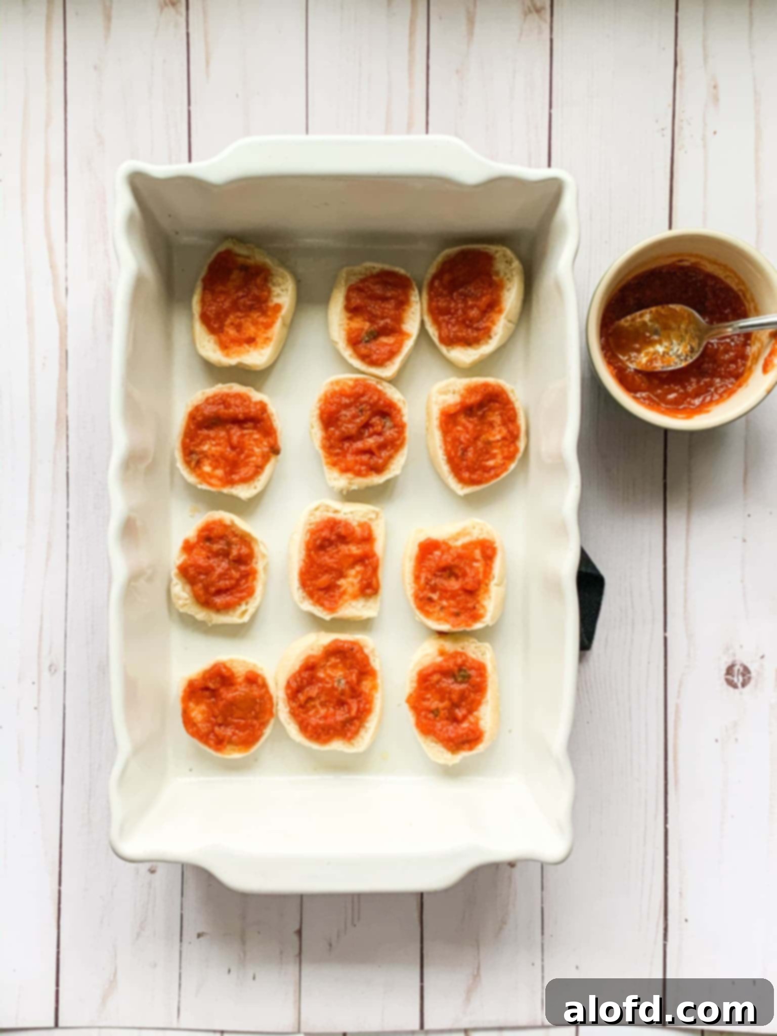 Zesty Italian Slider Bites 7 spreading marinara sauce on mini slider buns inside a baking dish.