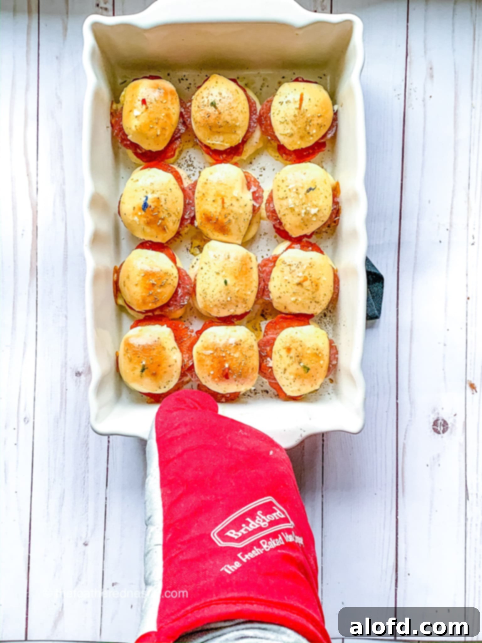 Zesty Italian Slider Bites 10 Hand covered with an oven mitt holding pan of hot Italian game day sliders