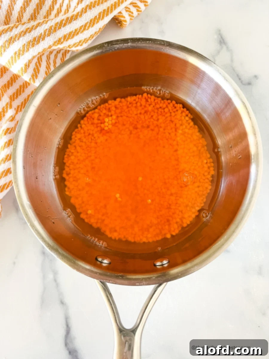 Red lentils simmering gently in a saucepan on a stovetop, with a spatula poised to stir, illustrating the traditional, controlled cooking method.
