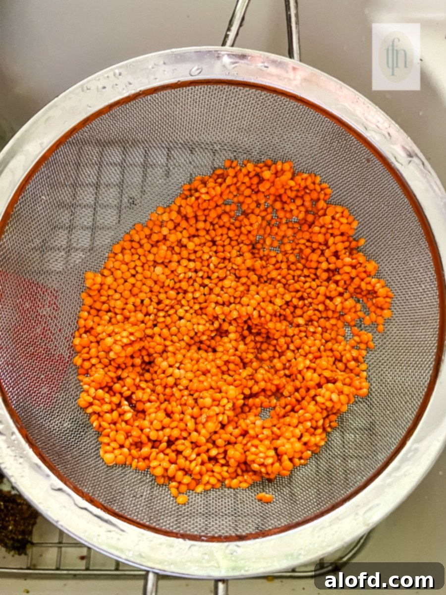 Cooked red lentils being strained through a fine mesh sieve, allowing any excess water to drain away, preparing them for immediate serving or further use.