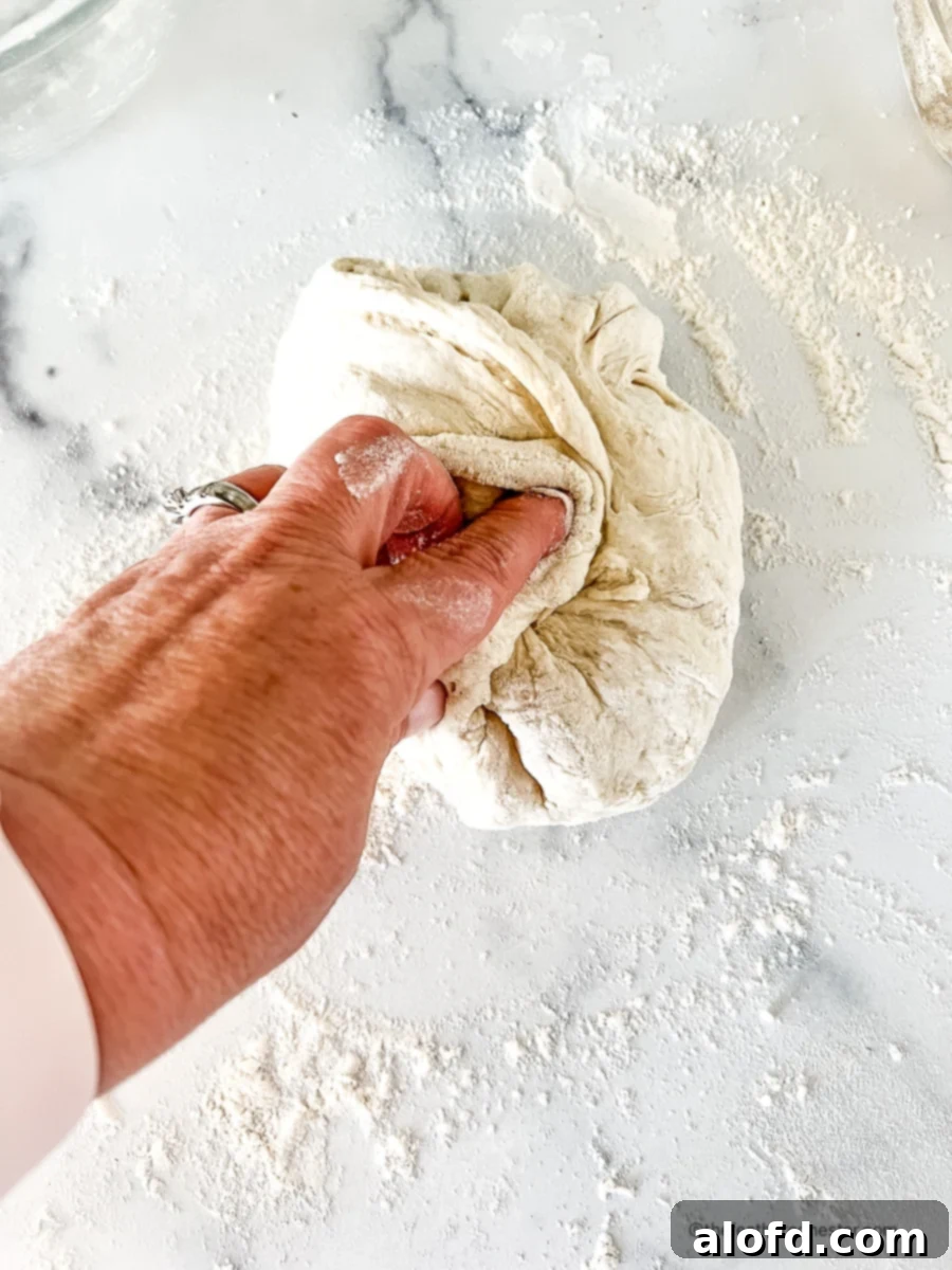 Foolproof Bisquick Pizza Dough 5 A hand gently kneading a portion of Bisquick pizza dough on a floured surface, demonstrating the initial shaping process.