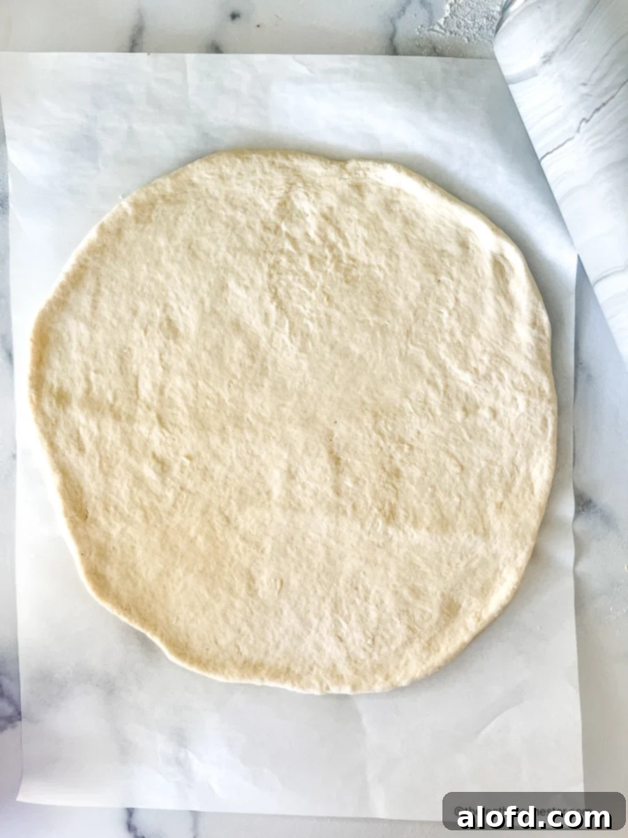 Foolproof Bisquick Pizza Dough 6 An unbaked Bisquick pizza dough crust, perfectly rolled out into a circle on a sheet of parchment paper, ready for toppings.