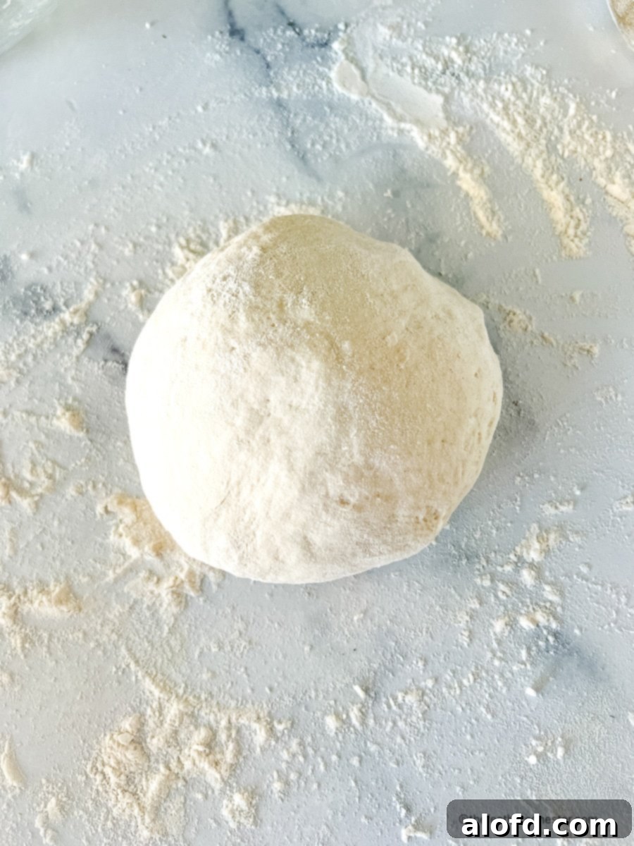 Foolproof Bisquick Pizza Dough 7 A perfect ball of Bisquick pizza dough on a floured marble surface, demonstrating ideal texture and readiness for rolling.