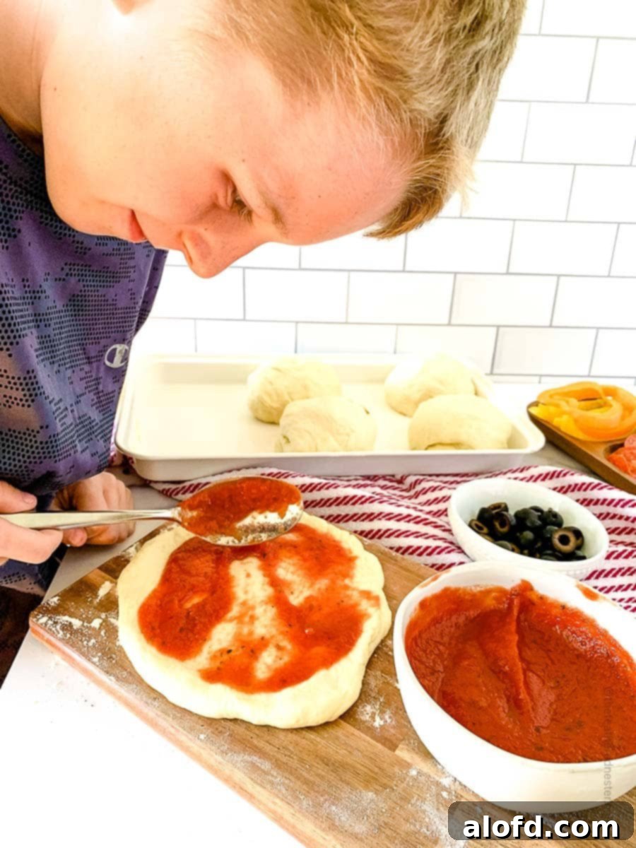 Foolproof Bisquick Pizza Dough 8 A young boy enthusiastically spreading pizza sauce onto a Bisquick pizza dough crust, demonstrating the fun and family-friendly aspect of making homemade pizza.