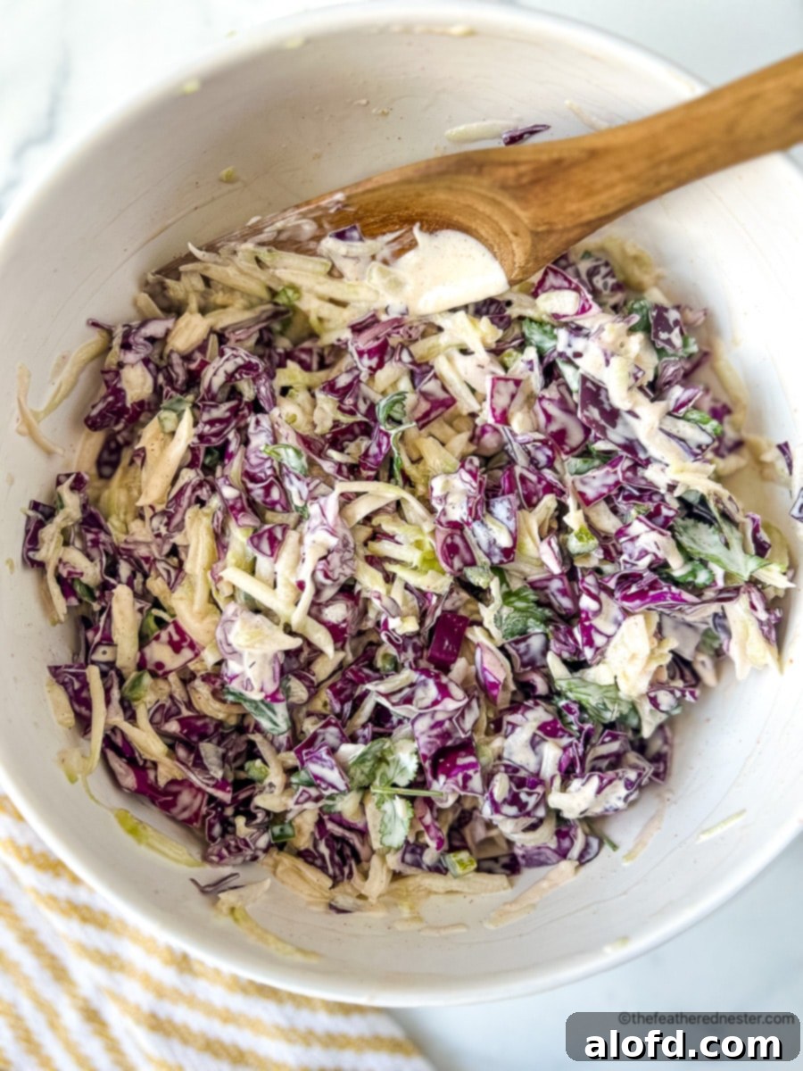 Mixing chopped red cabbage and cukes with creamy dressing in a large bowl.