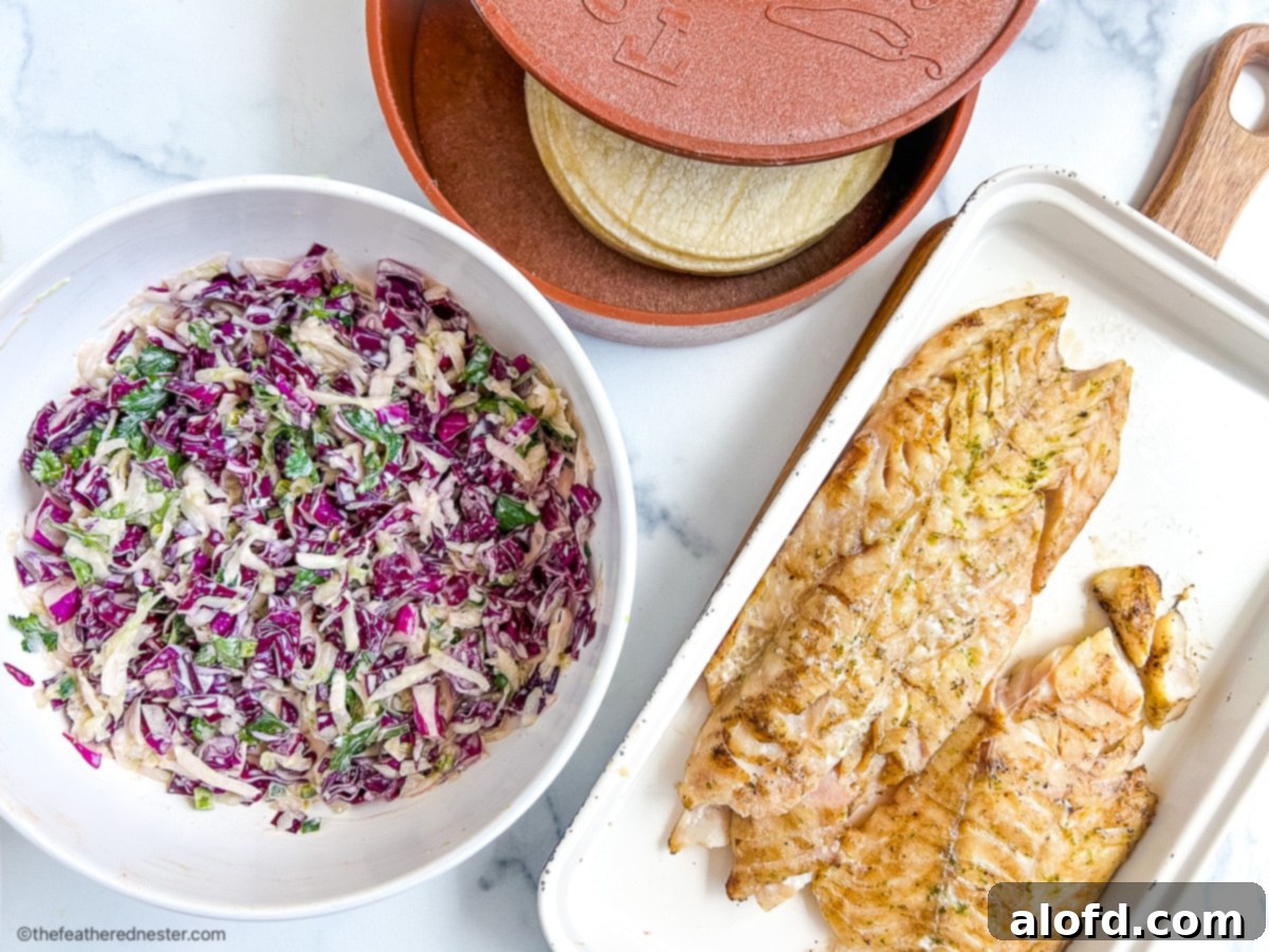 Bowl of slaw for fish tacos next to platters of grilled fish and corn tortillas.