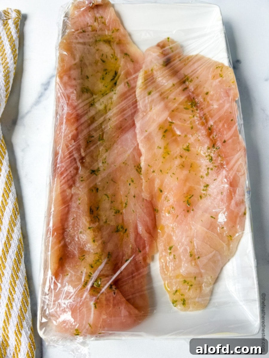 Two large Hawaiian rock cod filets on a white plate tightly wrapped in plastic wrap.