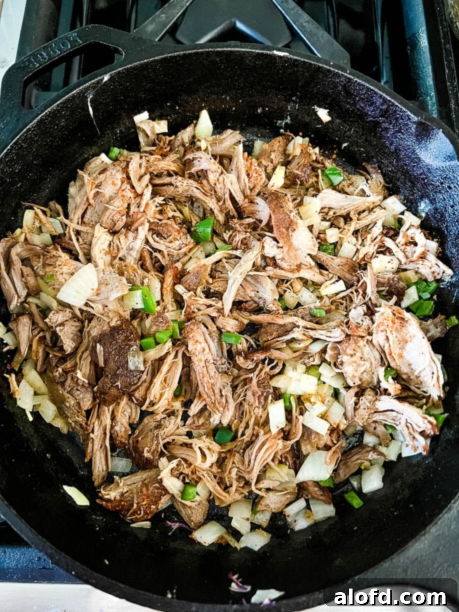 Cooking leftover pulled pork in a skillet with diced jalapenos and onions.