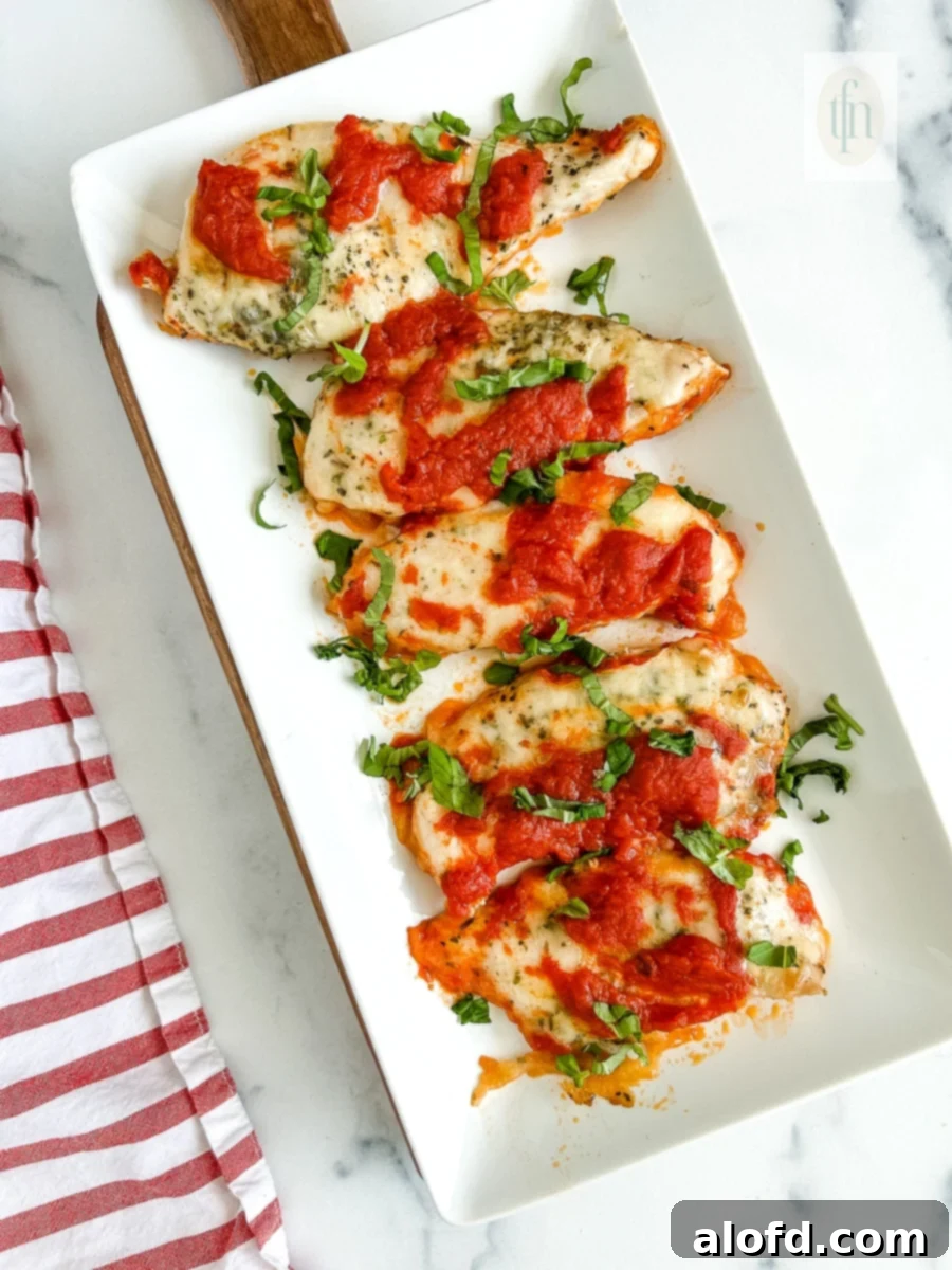 Golden-baked Italian chicken cutlets adorned with melted mozzarella, marinara, and fresh basil on a platter, ready for serving.