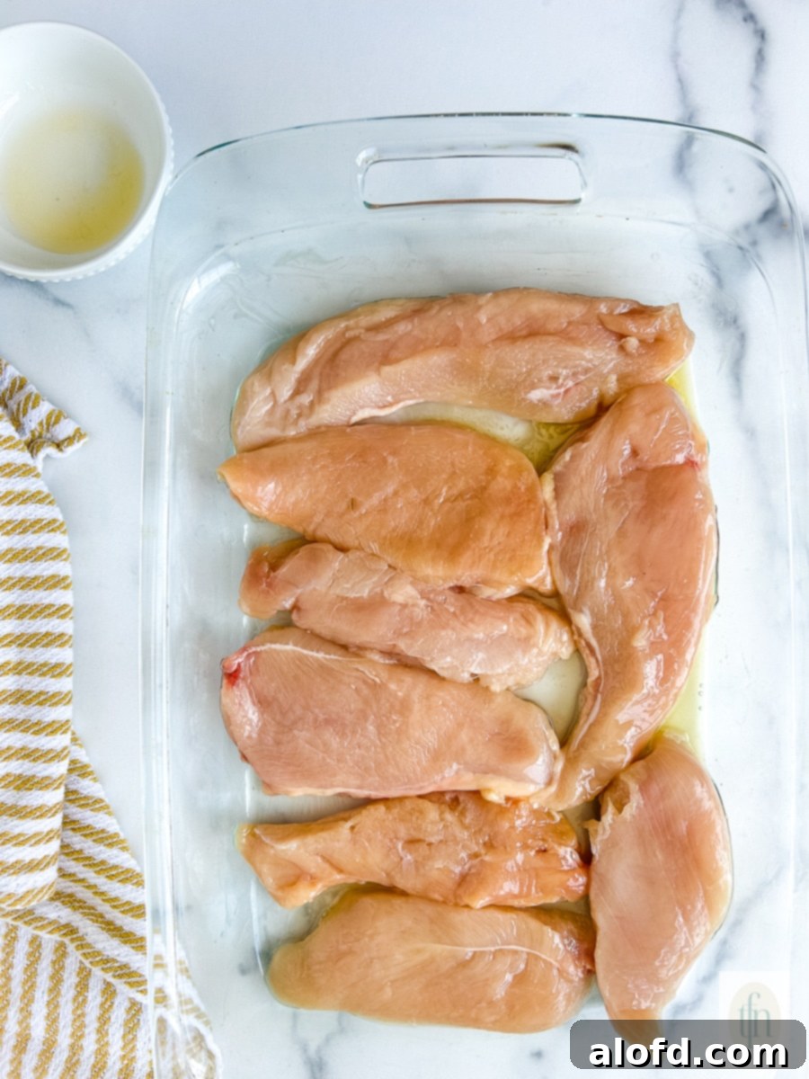 Uncooked thin chicken breast cutlets arranged in a baking dish, prepped for seasoning.