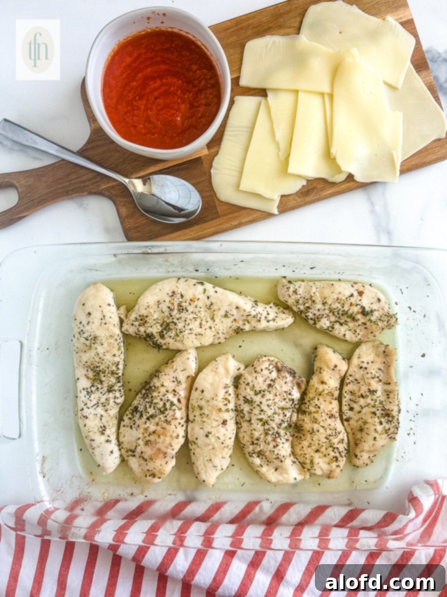 Lightly seasoned chicken cutlets baking in a glass dish, halfway cooked.