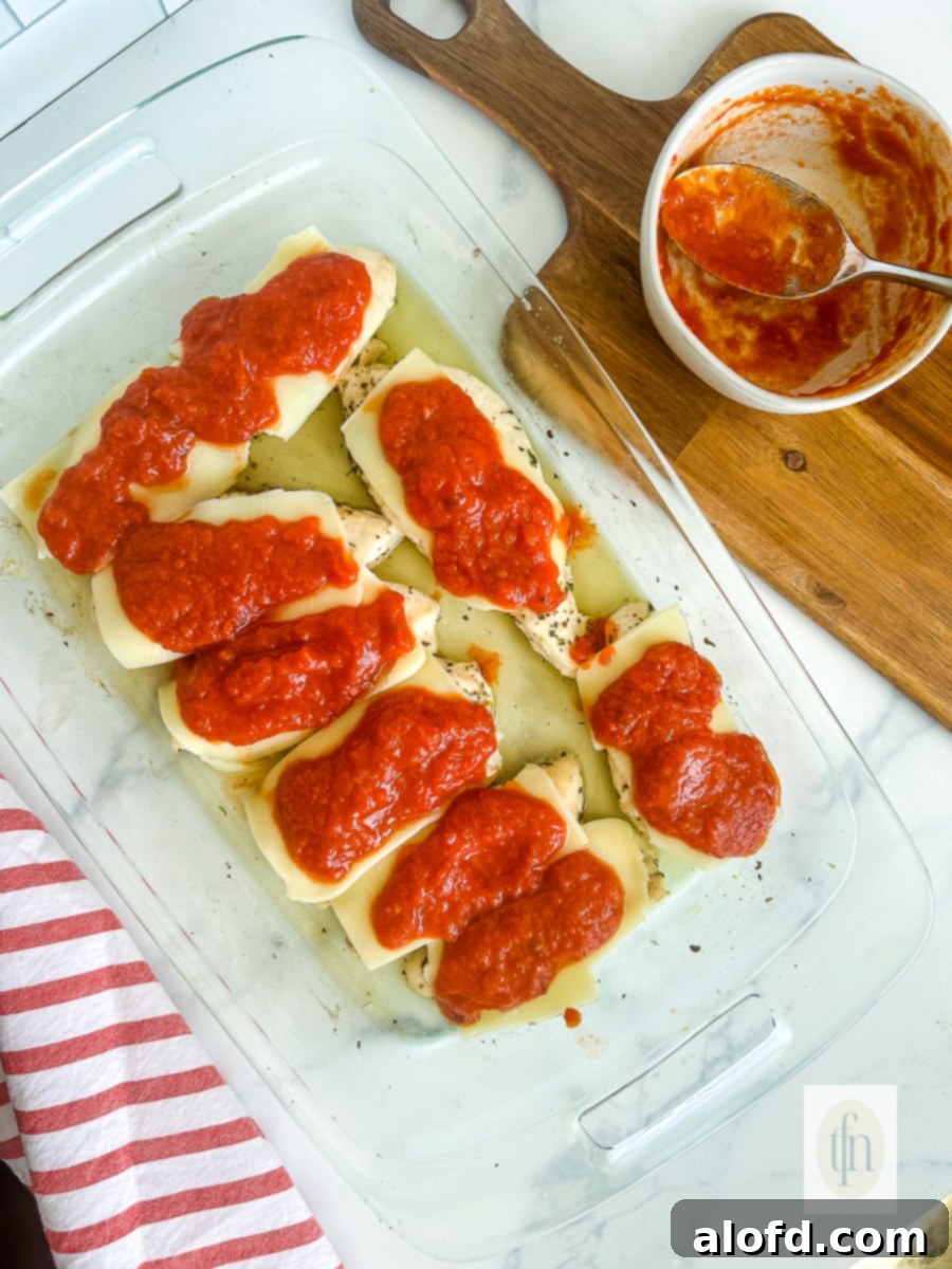 Melted mozzarella cheese topped with red marinara sauce in a casserole dish, ready for the final bake.