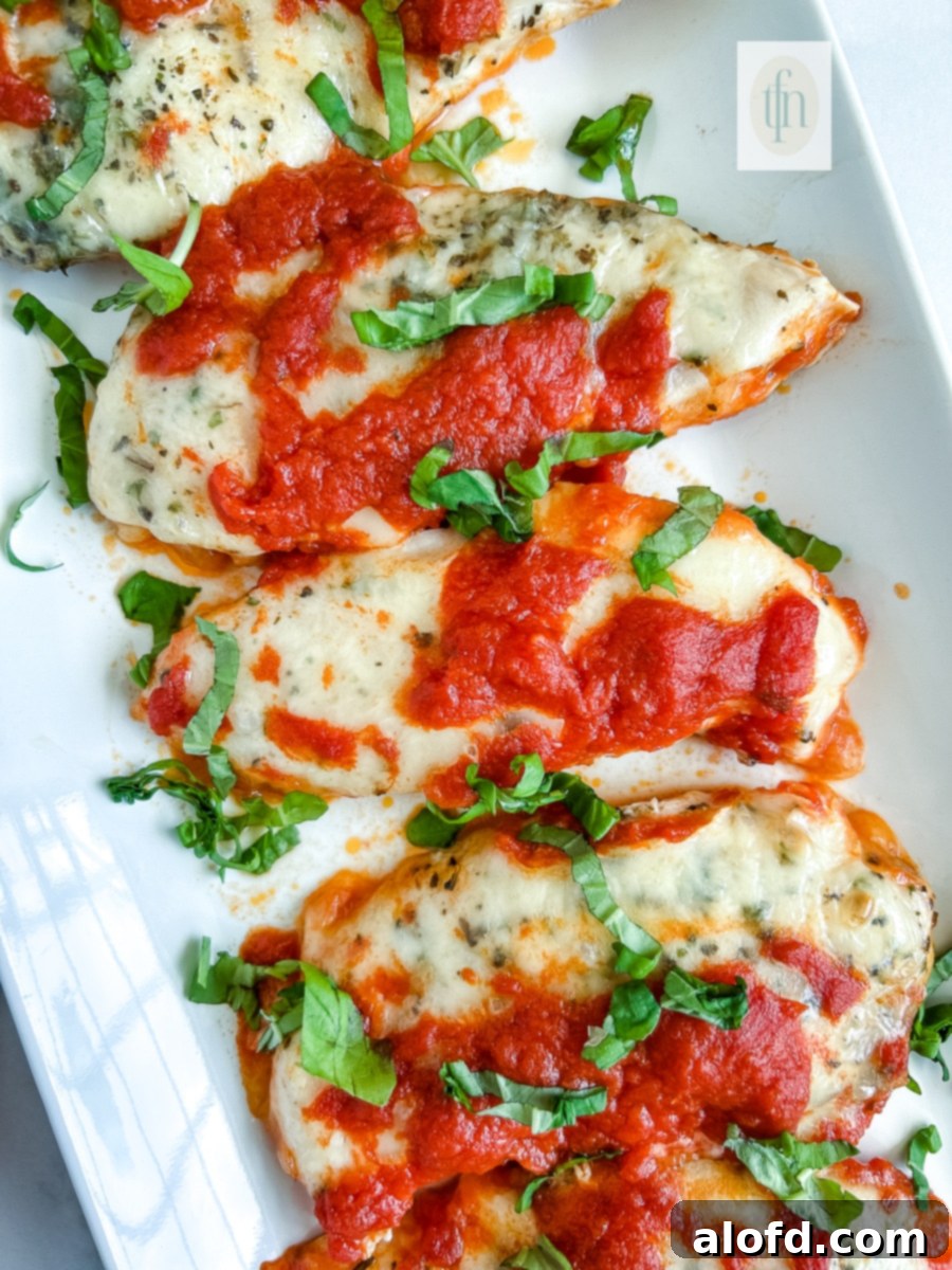 A close-up view of a baked Italian chicken cutlet on a white plate, showcasing the melted cheese, rich marinara, and fresh basil garnish.
