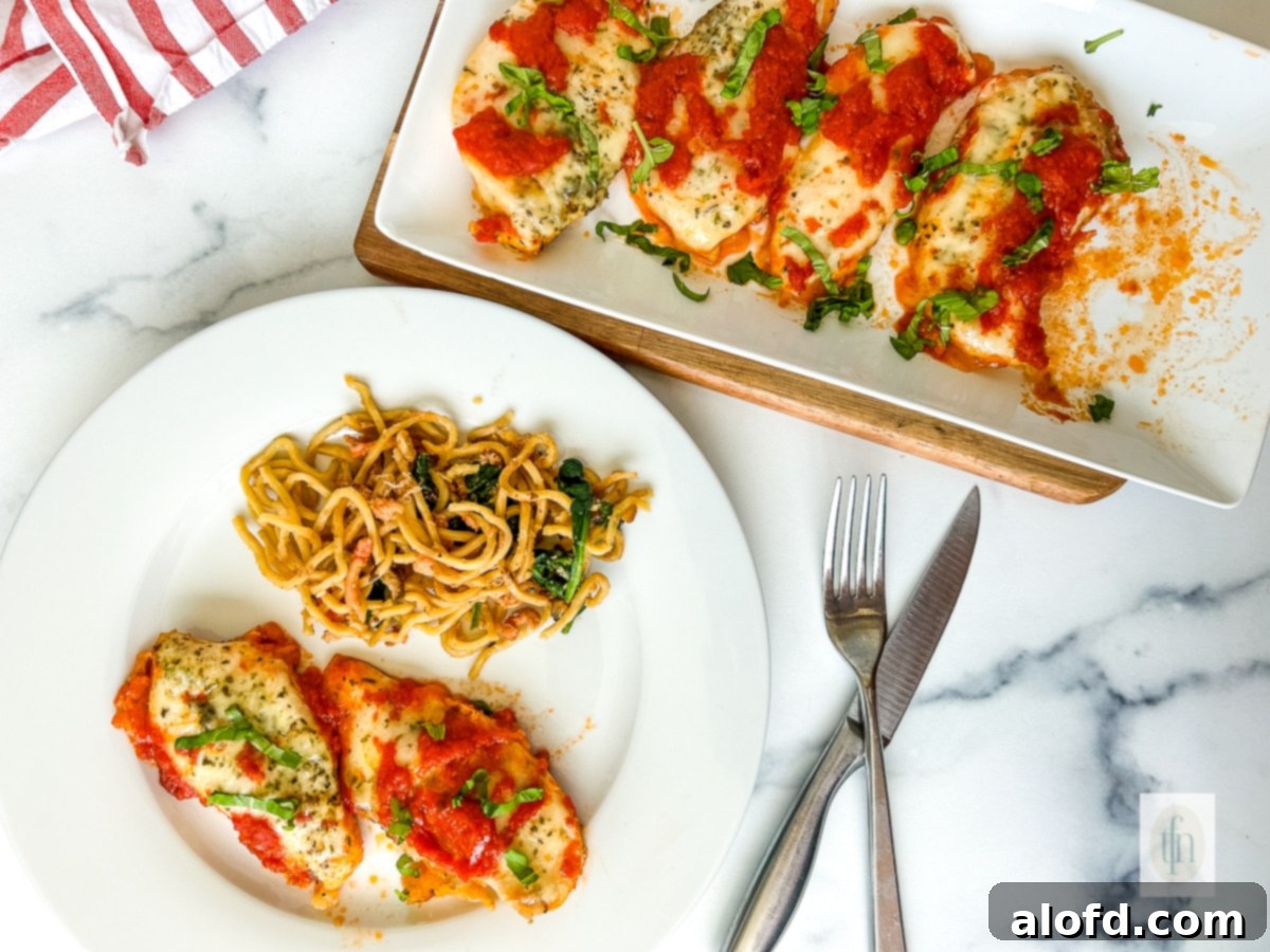 Italian baked chicken cutlets served on a white dinner plate, with additional cutlets on a larger serving platter in the background.