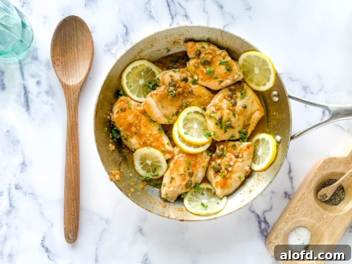 Homemade version of chicken piccata Cheesecake Factory recipe shown in a large skillet garnished with lemon slices and fresh parsley.
