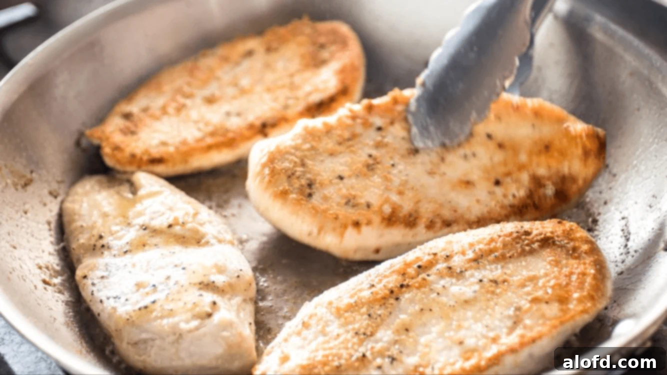 Searing chicken cutlets in a stainless steel skillet with olive oil.