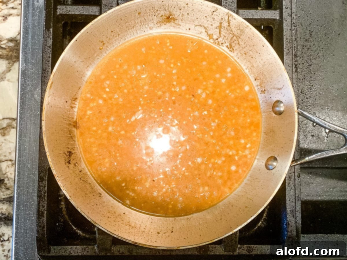 Creamy yellow lemon caper sauce simmering in a stainless steel skillet.