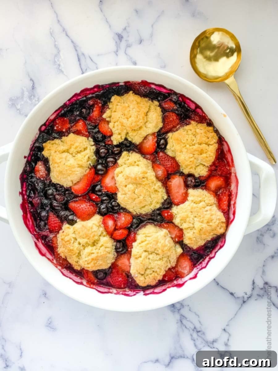 Effortless Bisquick Desserts for Every Event 4 a white casserole dish of baked strawberry blueberry cobbler ready to serve with a gold serving spoon