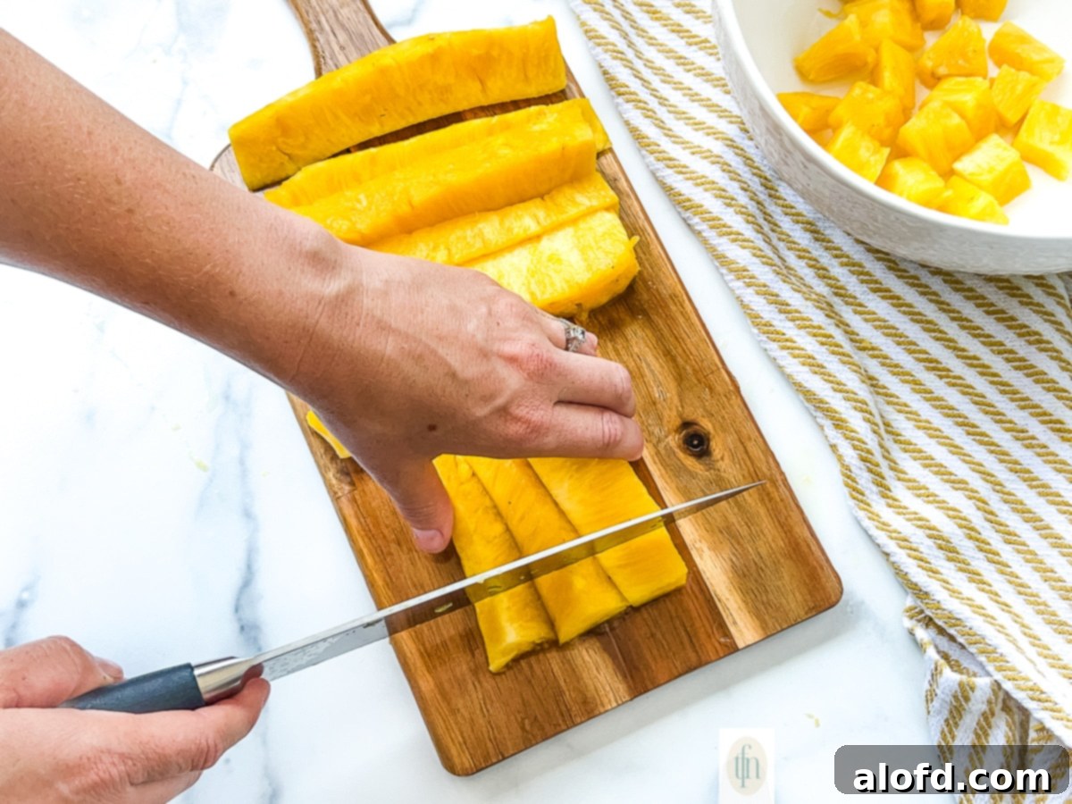A woman demonstrates how to core a pineapple and efficiently cut it into spears and chunks on a cutting board.