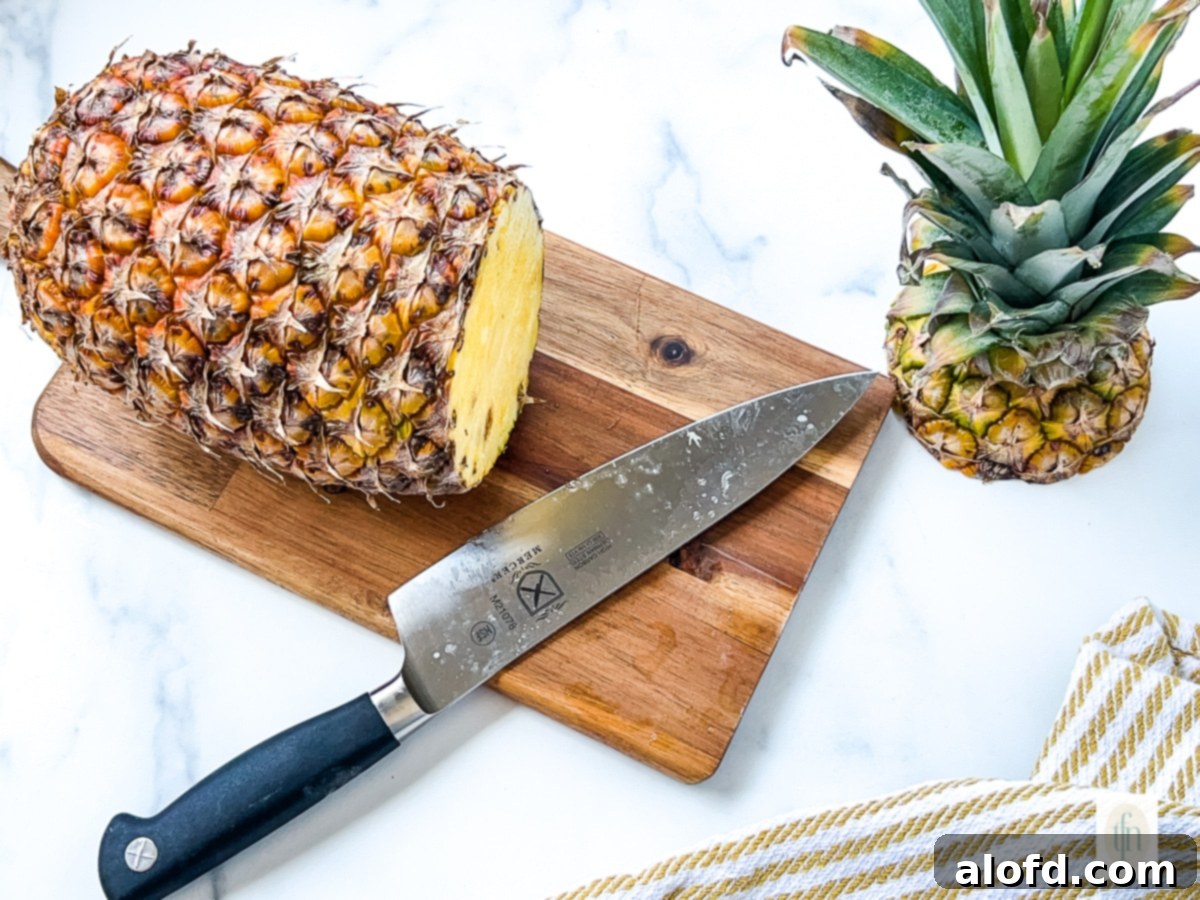 Top crown cut off of a whole pineapple, sitting next to the remaining fruit, illustrating the first step in preparation.