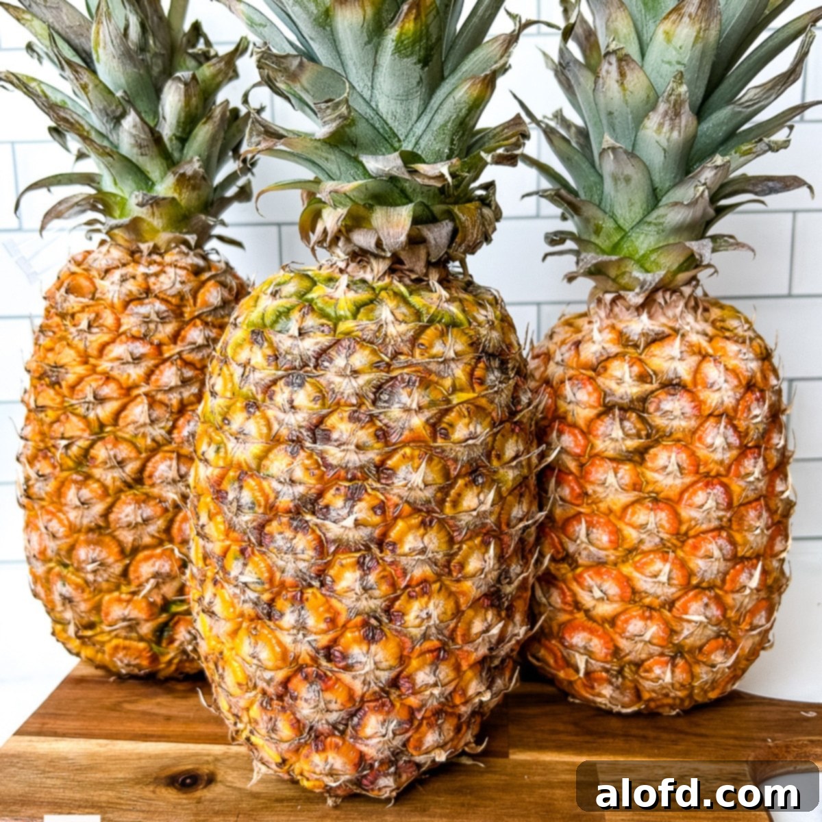 Three whole pineapples neatly arranged on a wooden cutting board, showcasing selection.