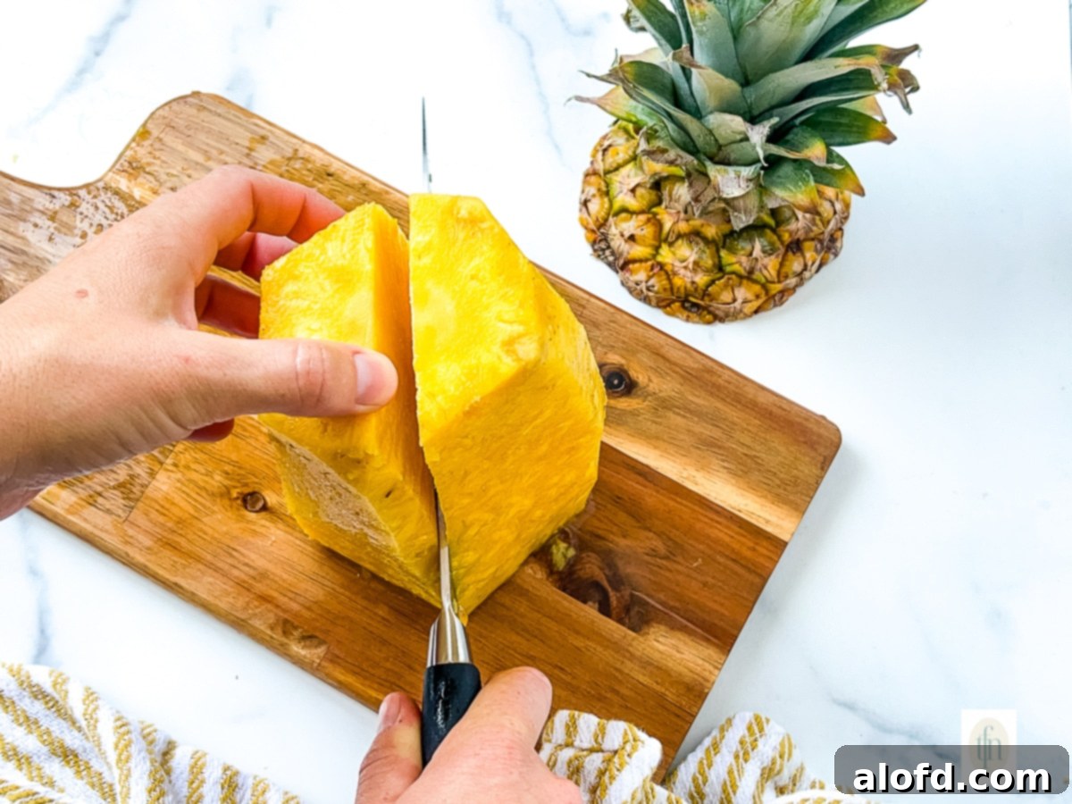 A freshly peeled pineapple, with some eyes removed, being cut into large wedges.